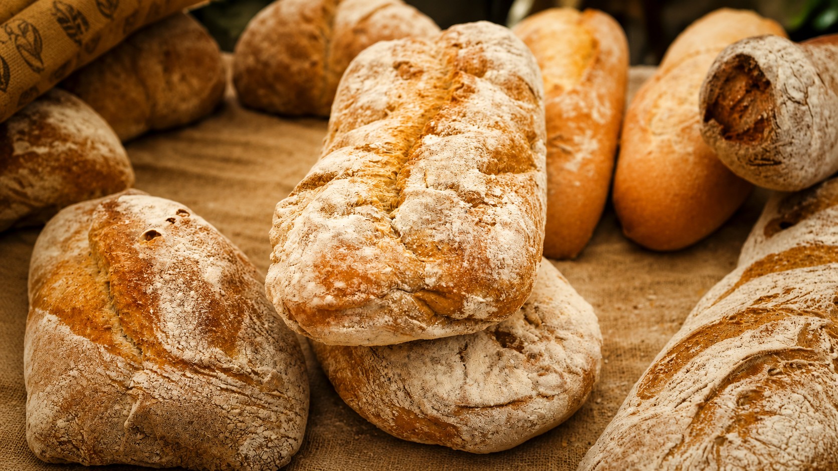 A rustic kitchen display featuring freshly baked, golden-brown sourdough loaves with detailed scoring patterns, set on a wooden surface alongside baking tools and flour.